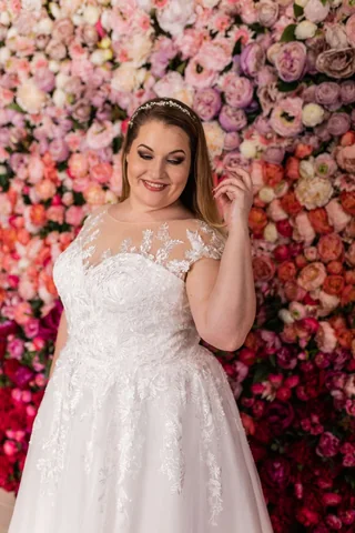 Lächelnde Plus-Size-Braut vor einer Wand aus rosafarbenen Blüten